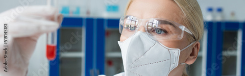 Scientist in protective mask holding blurred test tube in laboratory, banner.