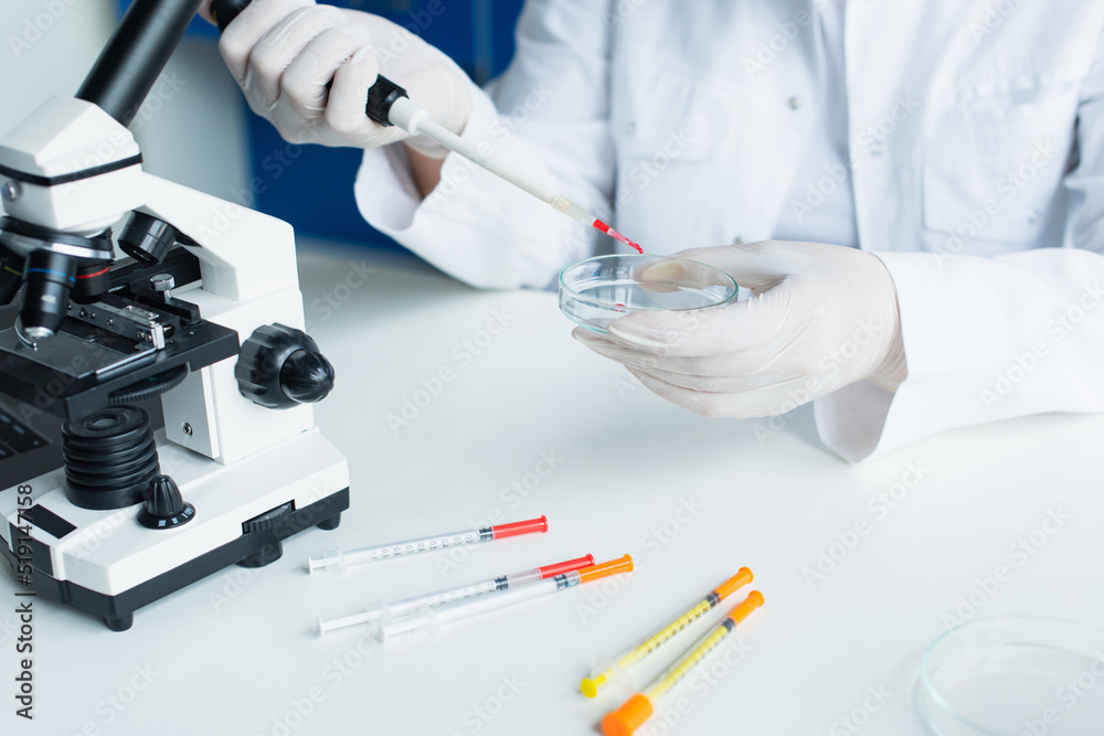 Cropped view of scientist working with electronic pipette and petri dish near microscope in lab.