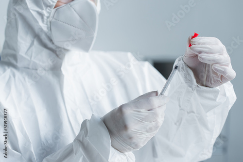 Cropped view of scientist in hazmat suit in latex gloves holding syringe in lab.