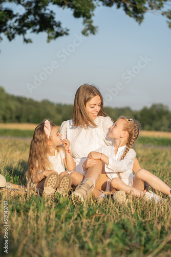 Mother and daughters relax in nature. Vertical photo of a mother with children. Family photo shoot in the village in the field. Psychology of the relationship between mother and child