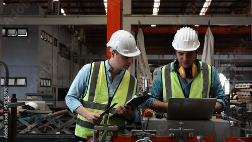 Two specialists inspect commercial, Wear safety uniform and White helmet work on laptop computer and clipboard. Two American people technician and Worker talk on a radio meet in a factory.