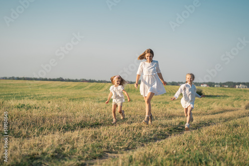 World Women's Day. A happy mother with her daughters runs into the field. Psychology of the relationship between mother and daughter. Life in a modern village