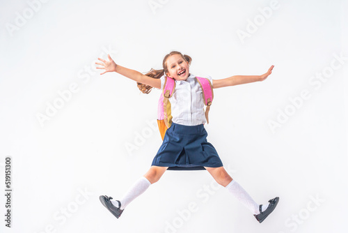 happy schoolgirl in uniform with a backpack jumps on a white background in the studio. the little girl is ready for school. conceptual school. the holidays begin. Advertising discounts