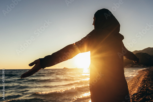Woman in hijab standing on the beach looking at horizon