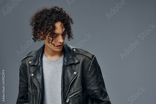 Serious adorable stylish tanned curly man leather jacket looks aside posing isolated on over gray studio background. Cool fashion offer. Huge Seasonal Sale New Collection concept. Copy space for ad