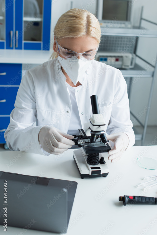 Scientist in protective mask working with microscope near laptop in laboratory. Scientist in protective mask working with microscope near laptop in laboratory.
