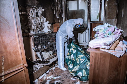 a specialist in a protective suit from a cleaning company cleans a destroyed housing after a fire