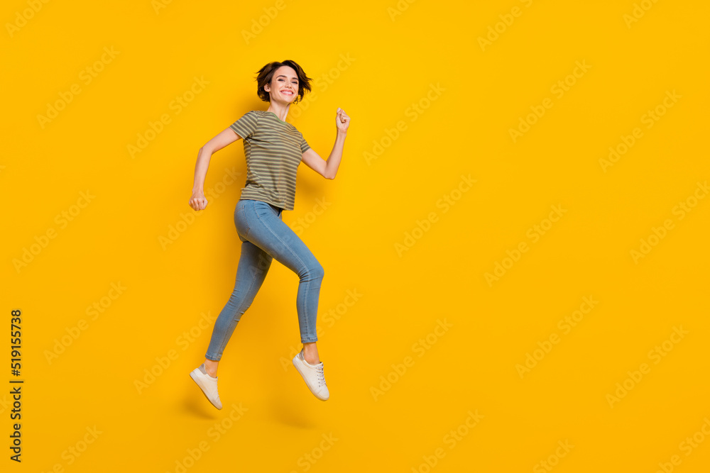 Full length photo of excited pretty girl dressed green t-shirt jumping high running empty space isolated yellow color background