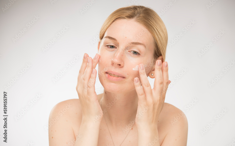 the girl rubs the cream on her face. happy blonde woman applies cream on face, makes face massage on white background isolated. the girl rubs the cream on her face. happy blonde woman applies cream on face, makes face massage on white background isolated.
