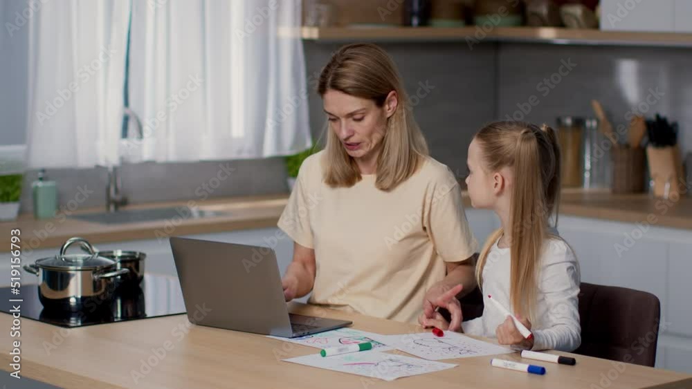 Stressful remote work. Busy mother freelancer typing on laptop at kitchen, little daughter disturbing her, free space Stressful remote work. Busy mother freelancer typing on laptop at kitchen, little daughter disturbing her, free space