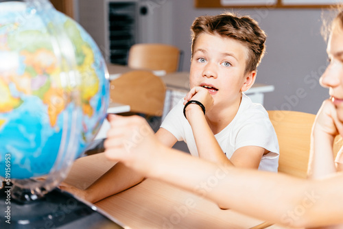 Cute pupil boy inquiringly looking at camera Children in school find something at the globe at classroom at school. Make the world a better place. photo