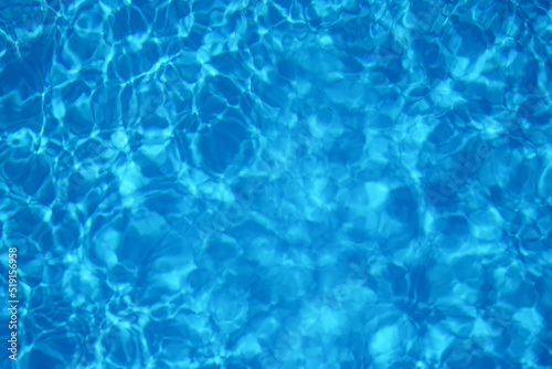Blue water in swimming pool with sun reflection, motion of ripple wave, top view.