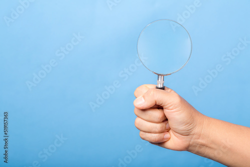 woman hand holding magnifying glass isolated on blue background. optical zoom lens is macro tool, concept for education, science.
