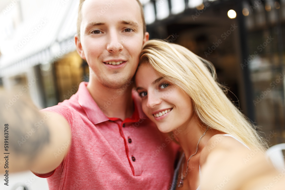 Smiling beautiful girl and her boyfriend in casual summer clothes. Happy family taking selfie self portrait of themselves on smartphone camera. Having fun on the street background.