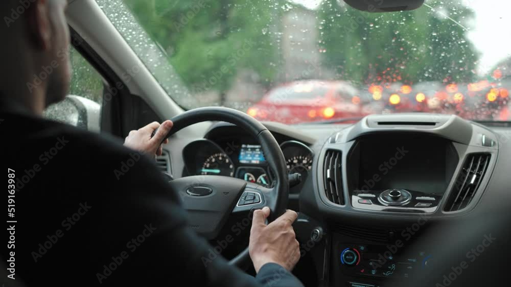 Man drives a car along the road in the city during the rain. View from behind the driver's shoulder
