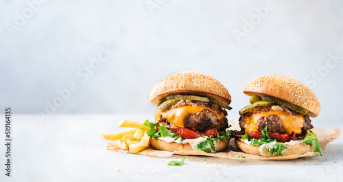 Two craft cheeseburgers and fries on parchment paper over grey concrete background. Copy space. Web banner burgers
