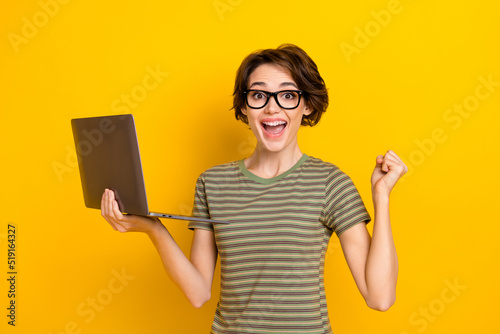 Photo of funny lucky girl dressed green t-shirt eyewear rising fist chating modern gadget isolated yellow color background