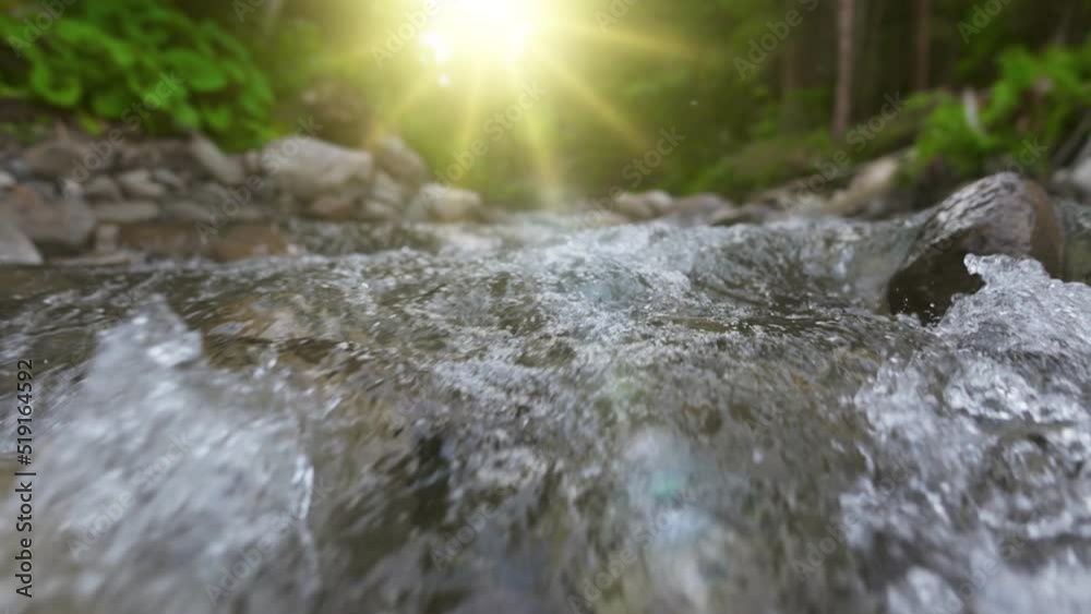 Fast mountain river in the forest. Camera moves along the surface of the water and stones, setting sun and greenery in the background. Slow motion UHD shot