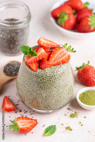 Chia pudding with green tea matcha powder and strawberries in a glass on pink background
