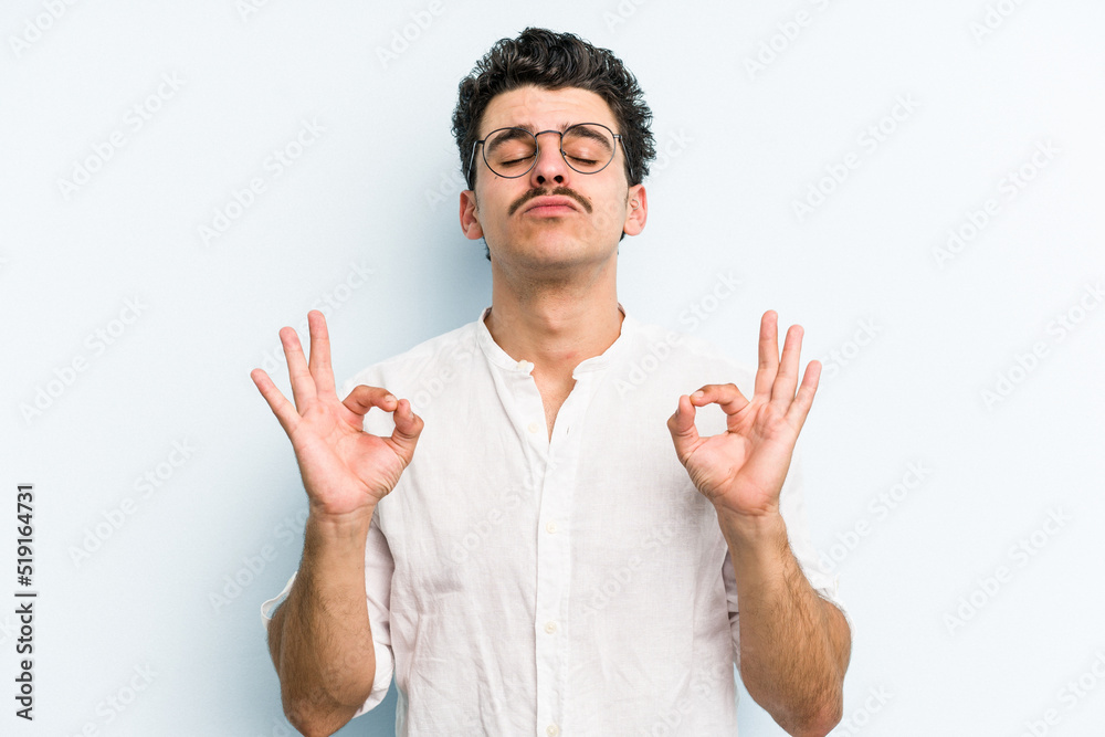 Fototapeta premium Young caucasian man isolated on blue background relaxes after hard working day, she is performing yoga.