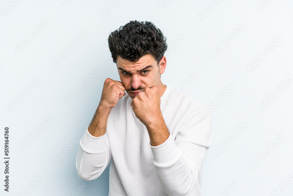 Young caucasian man isolated on blue background throwing a punch, anger, fighting due to an argument, boxing.