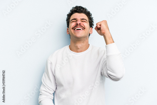 Young caucasian man isolated on blue background celebrating a victory, passion and enthusiasm, happy expression.