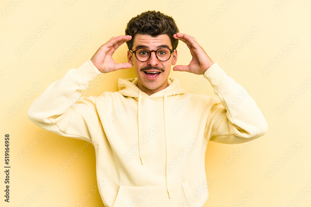 Young caucasian man isolated on yellow background receiving a pleasant surprise, excited and raising hands. Young caucasian man isolated on yellow background receiving a pleasant surprise, excited and raising hands.