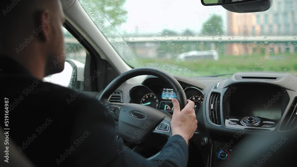 Man drives a car along the road in the city during the rain. View from behind the driver's shoulder Man drives a car along the road in the city during the rain. View from behind the driver's shoulder