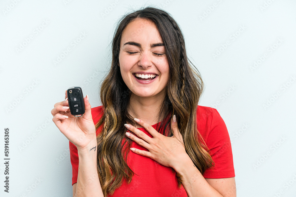 Young caucasian woman holding car keys isolated on blue background laughs out loudly keeping hand on chest. Young caucasian woman holding car keys isolated on blue background laughs out loudly keeping hand on chest.