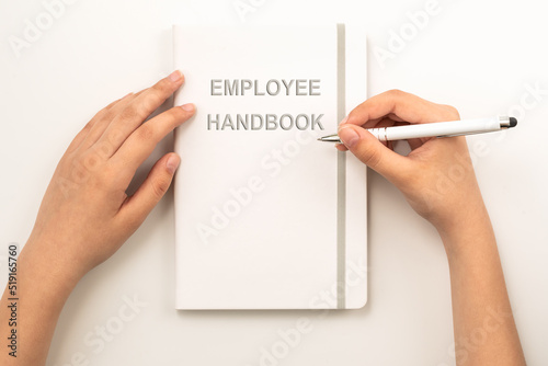 Female hands holding white Employee Handbookon grey background  top view 