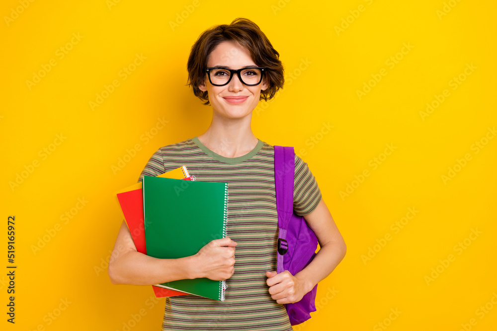 Photo of sweet cheerful girl dressed green t-shirt eyewear rucksack holding book isolated yellow color background Photo of sweet cheerful girl dressed green t-shirt eyewear rucksack holding book isolated yellow color background