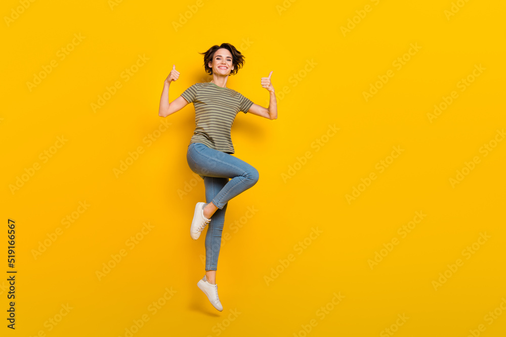 Full length photo of adorable confident girl dressed green t-shirt jumping thumbs up empty space isolated yellow color background