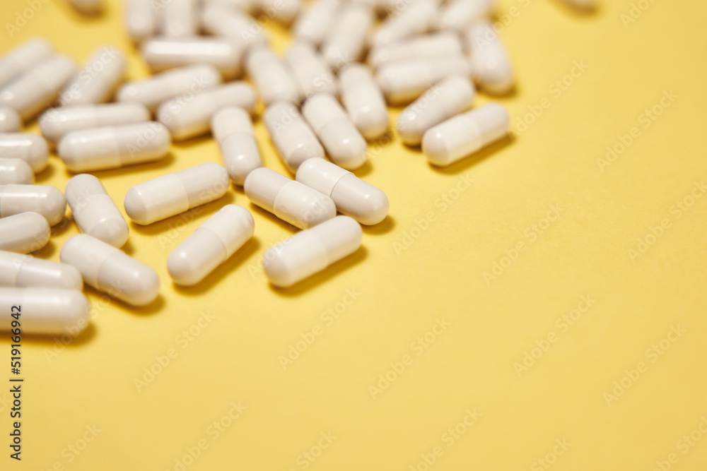 background with white pills. white capsules with medicine are scattered on a yellow background. vitamins, dietary supplements