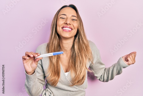 Beautiful hispanic woman holding pregnancy test result screaming proud, celebrating victory and success very excited with raised arm