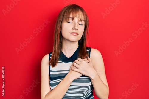 Redhead young woman wearing casual t shirt smiling with hands on chest with closed eyes and grateful gesture on face. health concept.