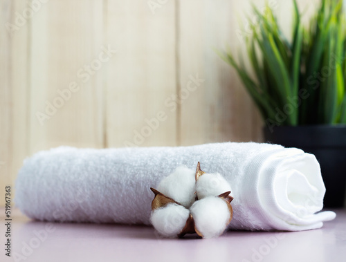 Rolled white towel with cotton flower on the pink table with wooden background