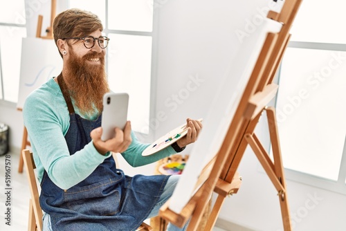 Young redhead man smiling confident drawing and using smartphone at art studio