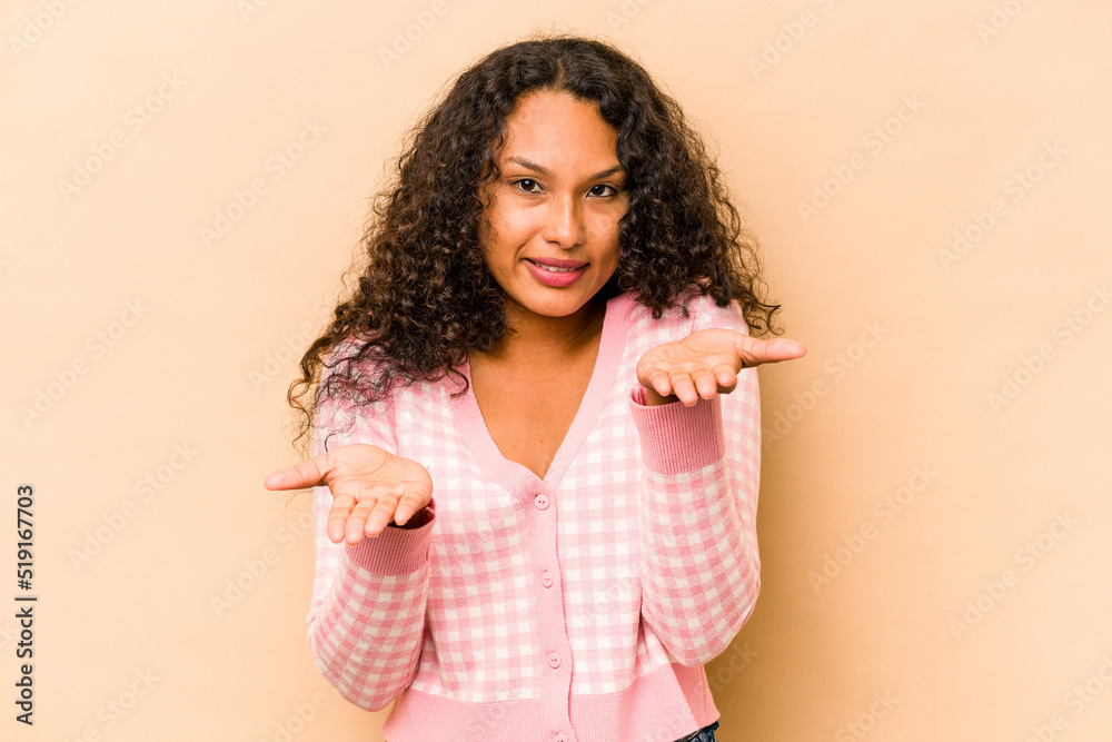 Young hispanic woman isolated on beige background makes scale with arms, feels happy and confident. Young hispanic woman isolated on beige background makes scale with arms, feels happy and confident.