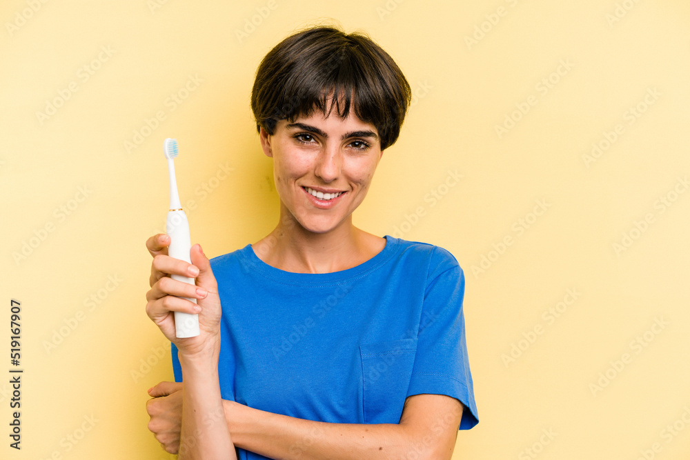 Young caucasian woman holding a electric toothbrush isolated on yellow background laughing and having fun. Young caucasian woman holding a electric toothbrush isolated on yellow background laughing and having fun.