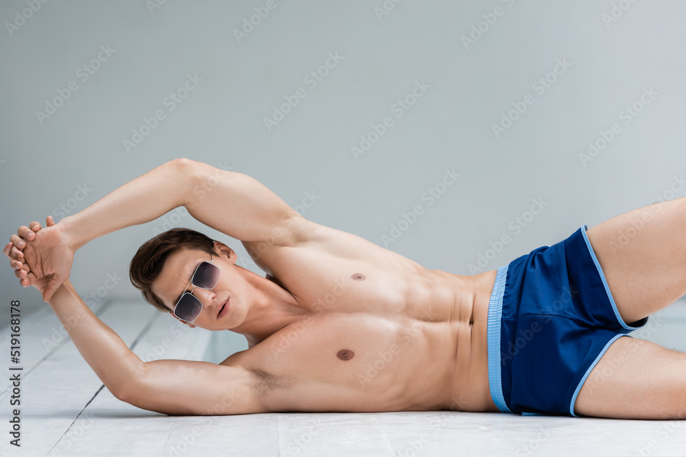 Fototapeta premium athletic man in sunglasses and swimming trunks lying at poolside and stretching arms.