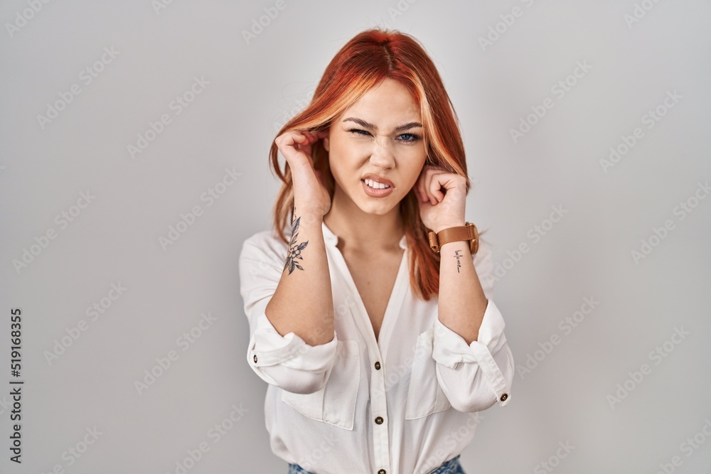 Young caucasian woman standing over isolated background covering ears with fingers with annoyed expression for the noise of loud music. deaf concept. Young caucasian woman standing over isolated background covering ears with fingers with annoyed expression for the noise of loud music. deaf concept.