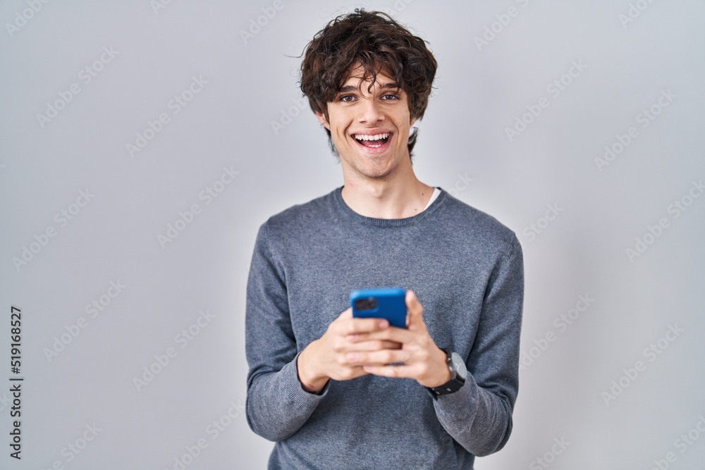 Young man using smartphone typing a message smiling with a happy and cool smile on face. showing teeth. Young man using smartphone typing a message smiling with a happy and cool smile on face. showing teeth.