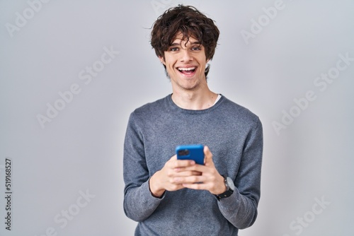 Young man using smartphone typing a message smiling with a happy and cool smile on face. showing teeth.