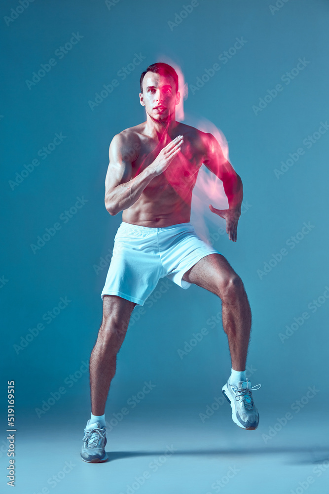 Dancing young guy with naked muscular torso performs zumba dance in neon light. Blurred motion. Sports workout