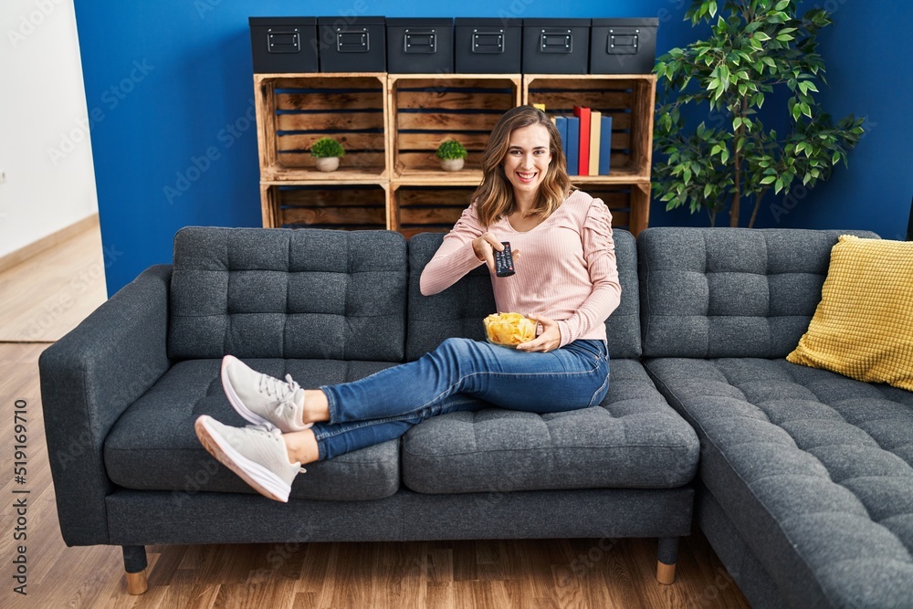 Obraz premium Young woman watching tv sitting on sofa at home