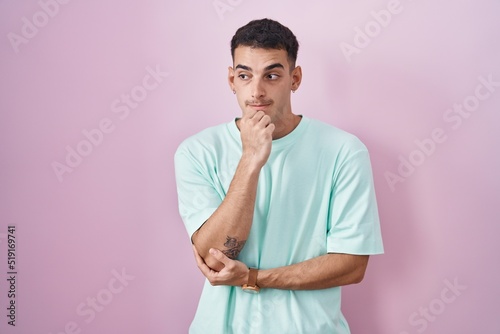 Handsome hispanic man standing over pink background looking stressed and nervous with hands on mouth biting nails. anxiety problem.