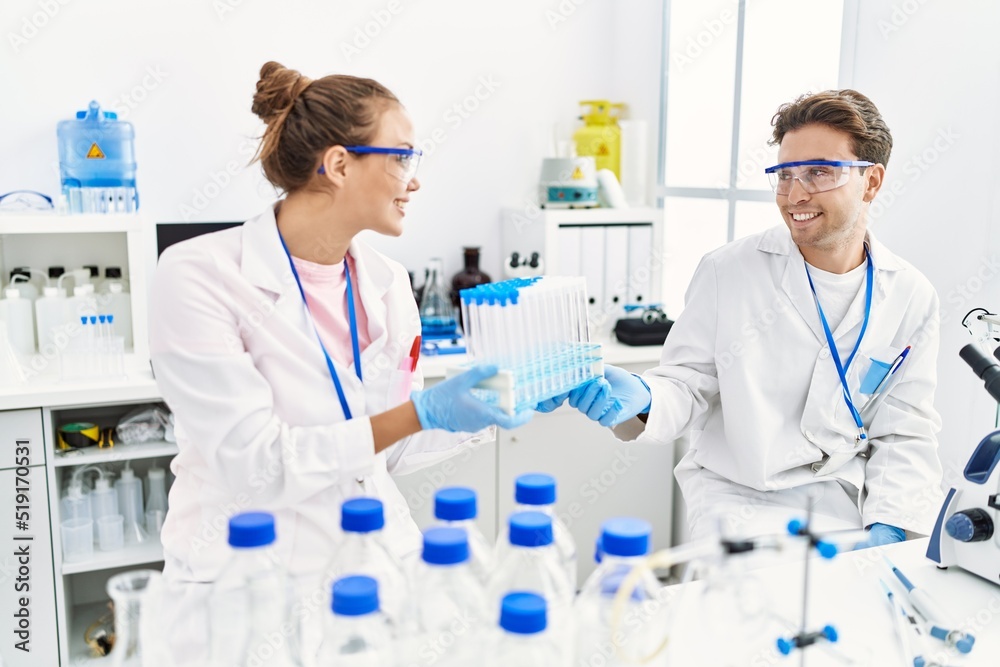 Man and woman wearing scientist uniform holding test tube at laboratory Man and woman wearing scientist uniform holding test tube at laboratory