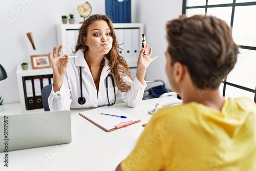 Young doctor woman showing electronic cigarette and normal cigarrete to patient puffing cheeks with funny face. mouth inflated with air  catching air.