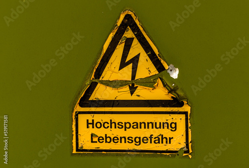 Weathered German sign: Hochspannung - Lebensgefahr, engl. high voltage - danger of life. High voltage symbol against green background.