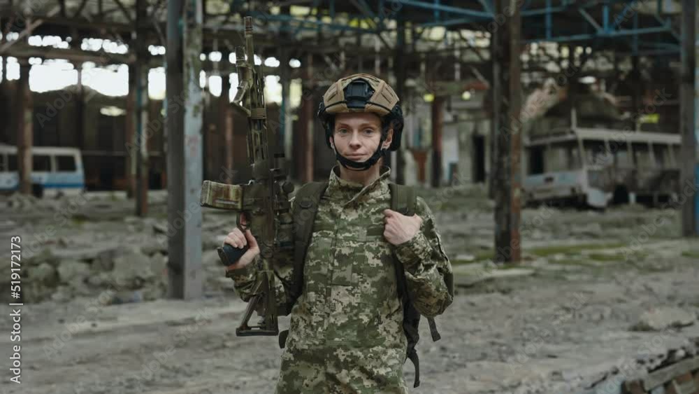 Portrait of fearless female fighter with weapon in hands confidently looking at camera while standing on industrial plant. Professionally trained soldier patrolling at destroyed factory during war. Portrait of fearless female fighter with weapon in hands confidently looking at camera while standing on industrial plant. Professionally trained soldier patrolling at destroyed factory during war.